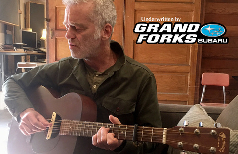Sean Hayes holding guitar with text in foreground: underwritten by Grand Forks Subaru