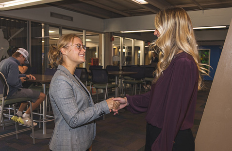 A business professional shaking hands with a student in an indoor setting.