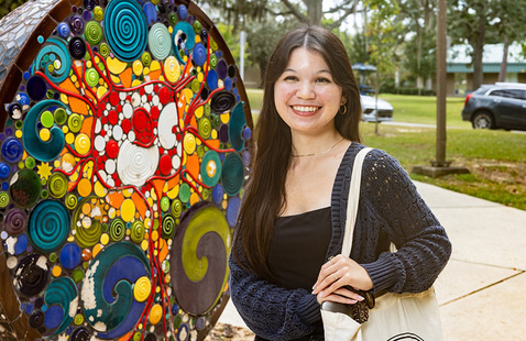 Student smiling at the camera while standing outdoors in front of a colorful spherical art installation.