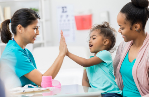 Little girl patient on mom's lap giving practitioner a high five