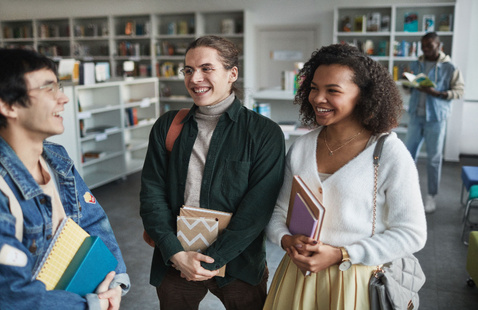 Group of diverse students laughing and holding books in a library environment.