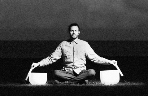 Photo of Jay Taylor with two sound bowls beside him in a crisscross style on the ground.