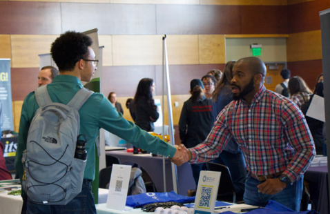 Student and potential employer shake hands at a career fair.