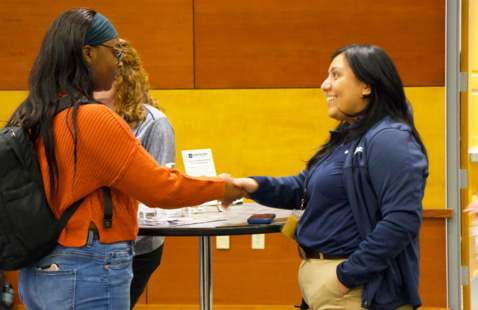 Student and potential employer shake hands at a career fair.