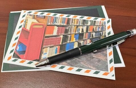 A Photo of a stack of postcards on a table with a pencil on top of the stack.