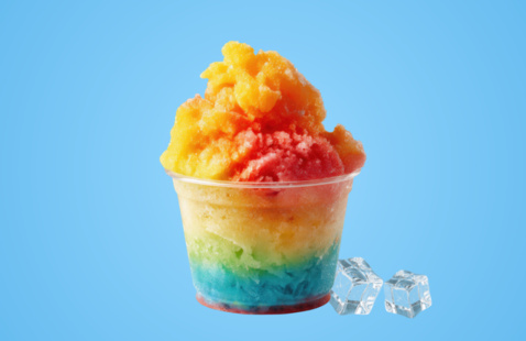 Cup of multi-colored shaved ice with two ice cubes next to cup