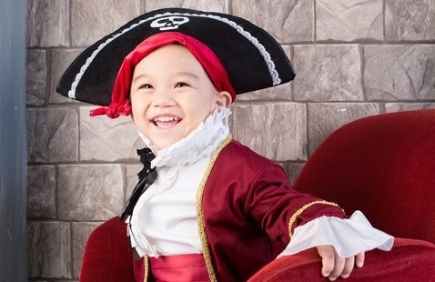 A child in a pirate costume smiling while sitting in a red chair.