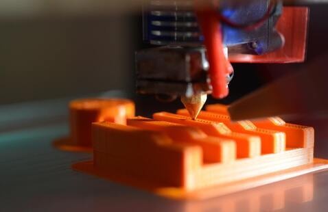 a close-up photo of a 3D printer printing an orange model.