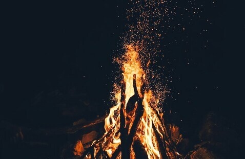 A campfire shining in the dark with sparks rising into the air. 