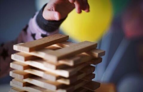 A child's hand reaching to stack some wooden rectangular "jenga-style" blocks. 