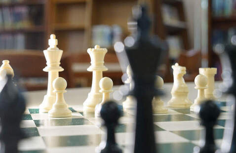 A close up view of a chess board from the perspective of the Black King gazing across the board at the opposing pieces