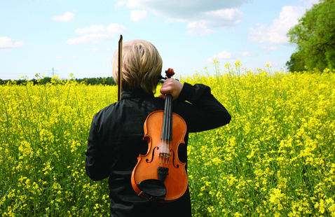 Young boy with violin walking through field of yellow wildflowers