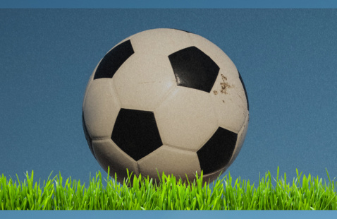 Soccer ball sitting on grass against blue background