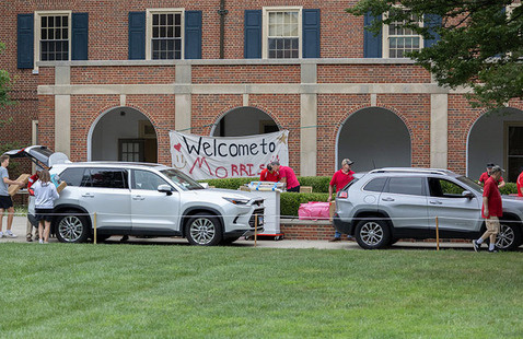 Move-in day at Morris hall with 2 cars unloading and a bedsheet sign with Welcome to Morris