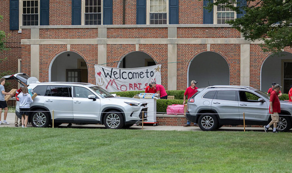 Move-in day at Morris hall with 2 cars unloading and a bedsheet sign with Welcome to Morris