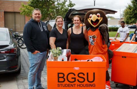 Student and family pose with Freddie Falcon beside a BGSU Student Housing move-in cart during campus move-in.