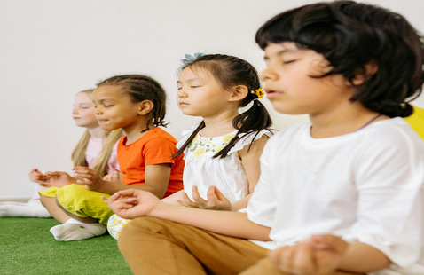Diverse group of children practicing meditation indoors in a classroom setting.
