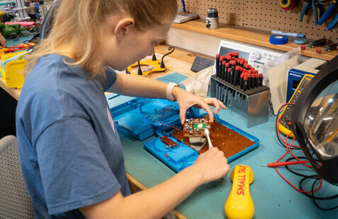 A woman uses tools to repair an electronic toy.