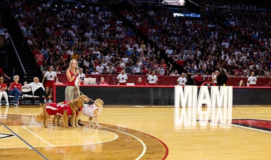 Renate Crawford and 3 golden retrievers on the basketball court at Millett talk to the crowd during convocation 2025 
