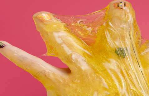 Detailed view of fingers with nail art covered in sticky yellow slime against a red background