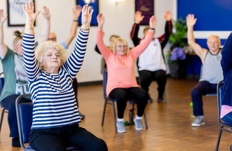 Group of senior adults participating in a chair exercise class, promoting fitness and healthy lifestyle