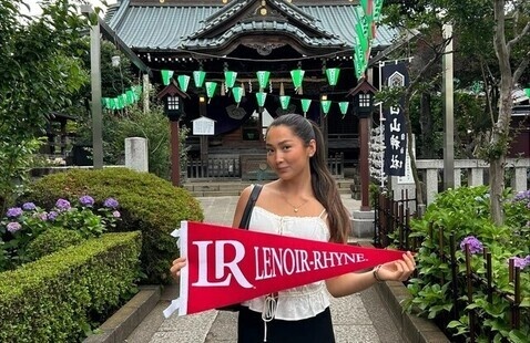 Student poses with an LR banner in front of a temple during an internship in Tokyo, Japan