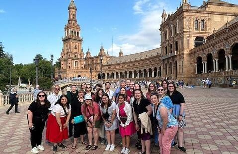 Faculty-led study abroad group pose for photo in historic plaza and building