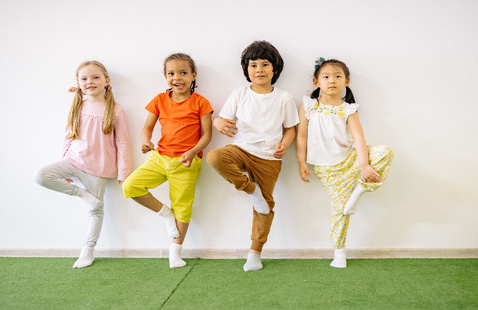 Four children joyfully participating in an indoor balancing exercise, promoting fun and fitness.