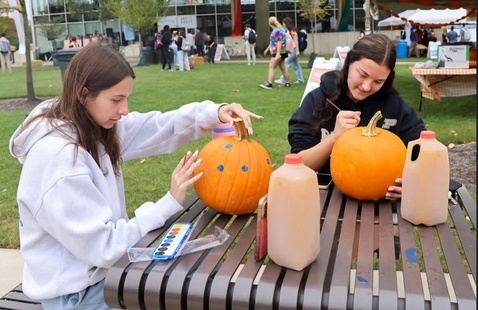 two students painting pumpkins with apple cider