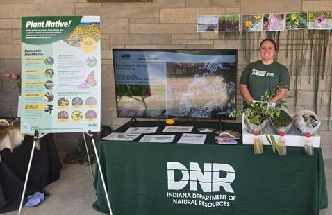 DNR staff member at a table with a screen and a poster that says "Plant Native!"