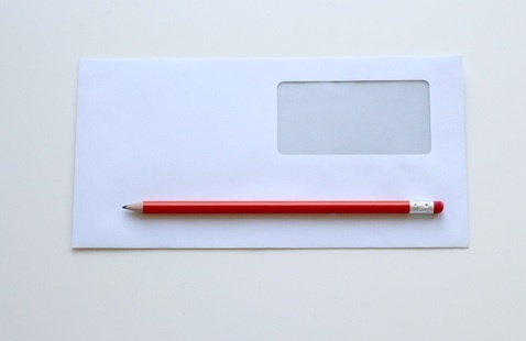 Photo of a white business envelope with a red pencil laid across it