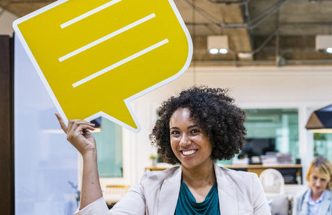 Photo of a smiling woman holding a cartoon, yellow speech bubble above her head
