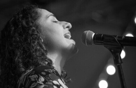 A woman sings into a microphone with her eyes closed. The photo is in black and white.