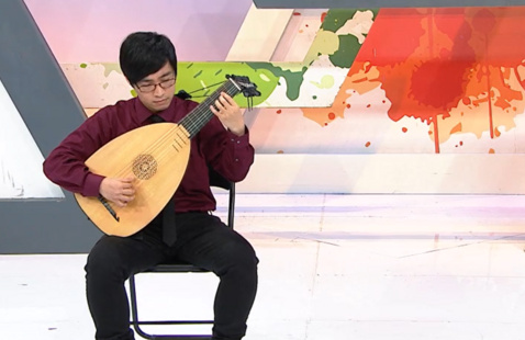 Guitarist and lutenist Kenneth Kam sits in a chair while playing a lute. The background is abstract and colorful.