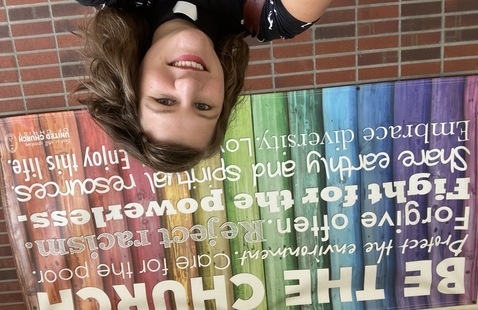 Photo of woman with multi-colored sign titled Be the Church