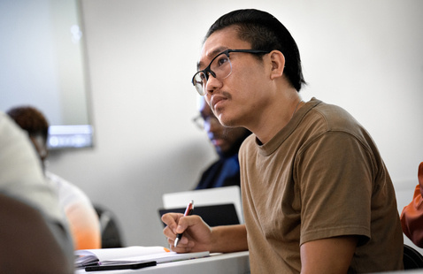 Student listens to professor lecture at desk in classroom
