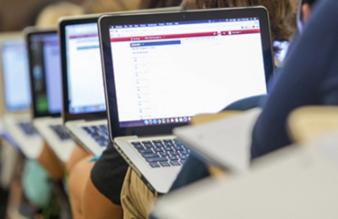 A row of students in a classroom with their laptops open