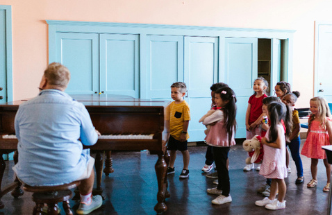 Children looking at adult playing the piano.