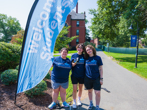 Smiling Orientation Leaders pose next to "welcome new students" sign.