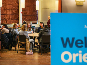 Students sit at tables in the Great Room, Orientation.