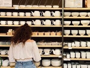 A person shopping, rows of cups and bowls on shelves.