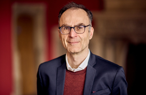 Professor Seena Fazel wearing glasses and a navy blazer against a softly blurred indoor background.
