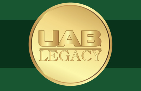 Circular gold medallion displaying the words “UAB Legacy” in embossed gold lettering, set against a green background with horizontal dark green bands.
