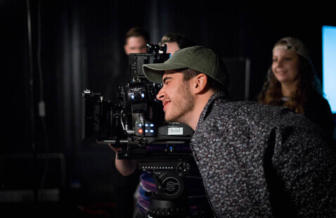 students in a filming class with equipment looking into a camera