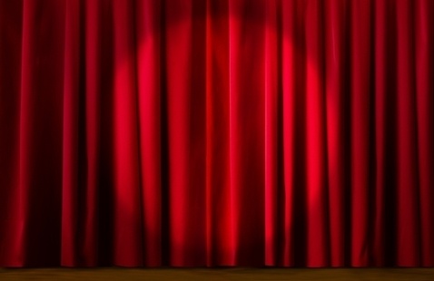 Closed red theater curtains hanging above a wooden stage floor