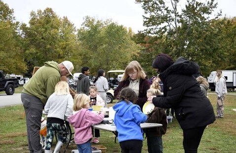 Kids and adults gathered around a table in the outdoors, making crafts.