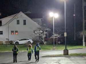 Photo of three students in high visibility vests walking away from the camera, into a large bright street light.