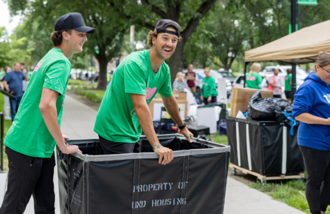 Two students pushing a cart to help students move in to their residence hall.