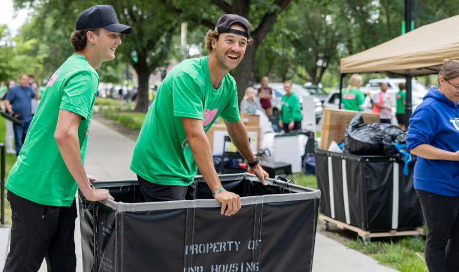 Two students pushing a cart to help students move in to their residence hall.
