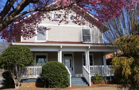 The Willson Center, a two-story grey house with a wide front porch. In the foreground is an overhanging bough of cherry blossoms.